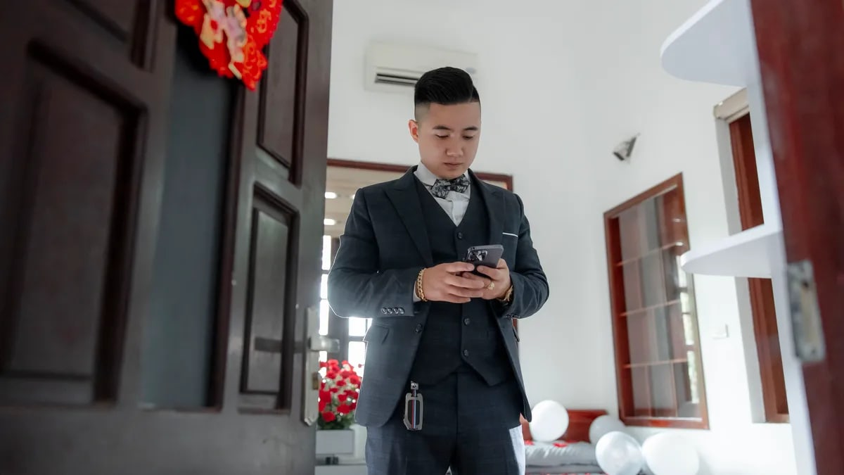 A groom in a suit checks his smartphone indoors, preparing for a wedding ceremony.